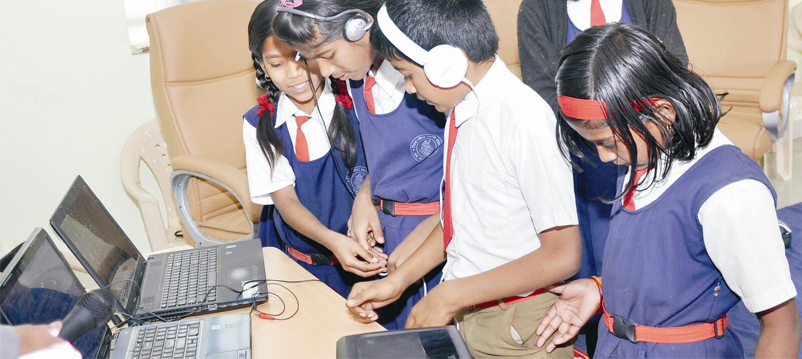 Students sharing headphones around a laptop during a live Global Classroom link-up.